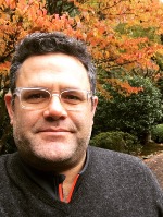 Matt smiling at the camera in a dark sweater with fall foliage in the background.