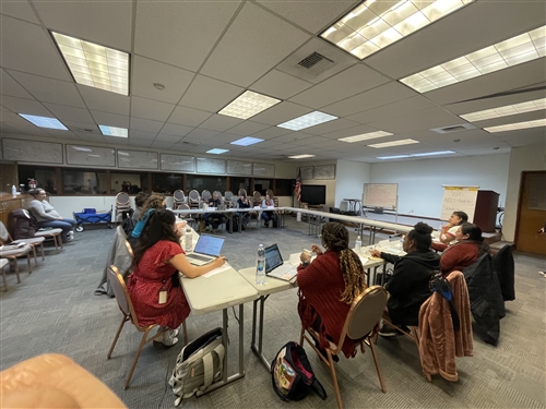 A board meeting in a circle of tables is shown in an office setting